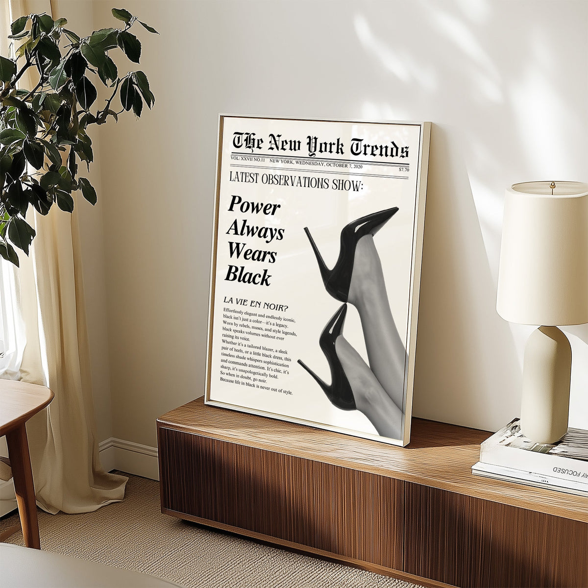 Two pairs of black heels mock newspaper print in a white frame on a walnut sideboard beside a ceramic lamp