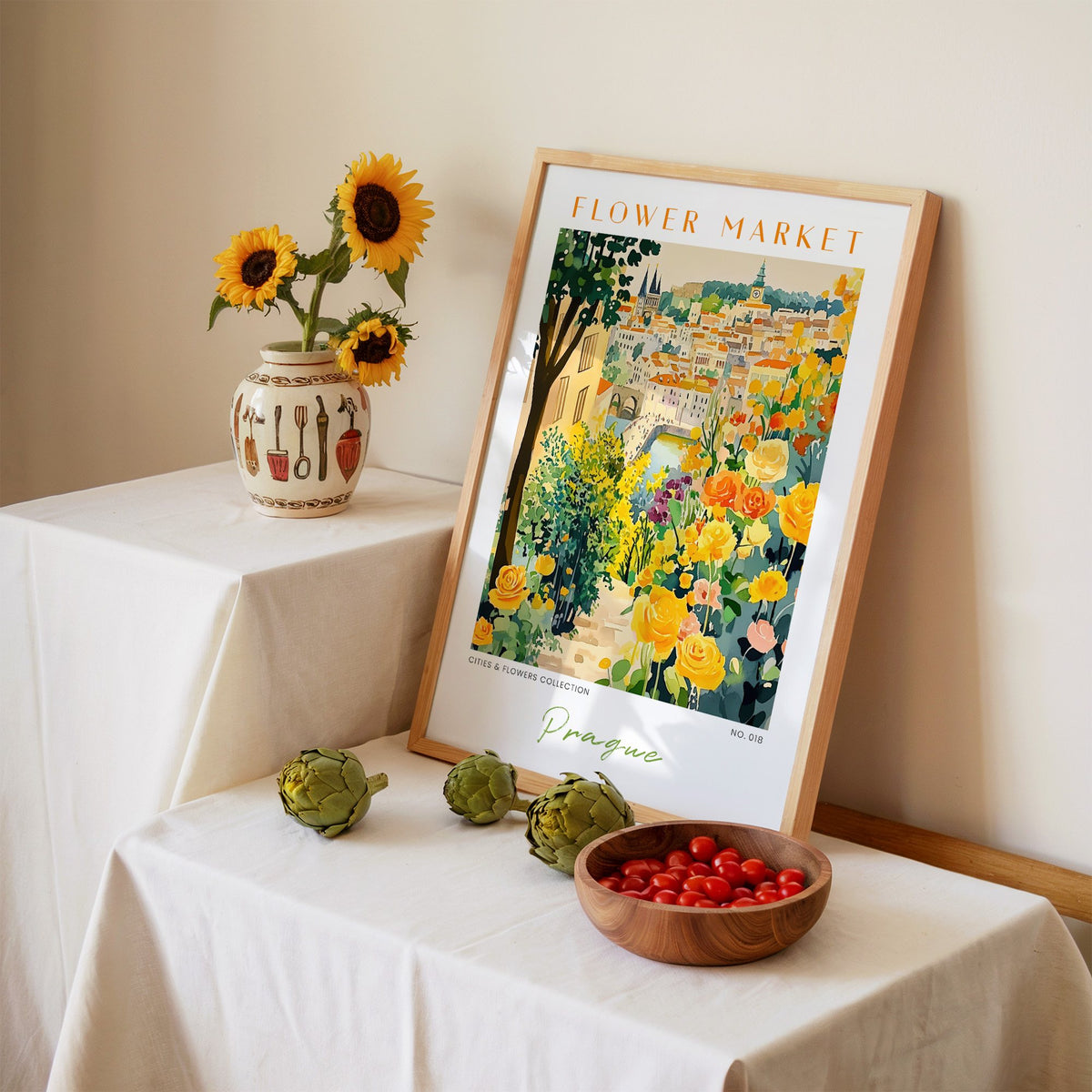 Prague flower market print in an oak frame leaning on a linen-draped table beside a vase of sunflowers