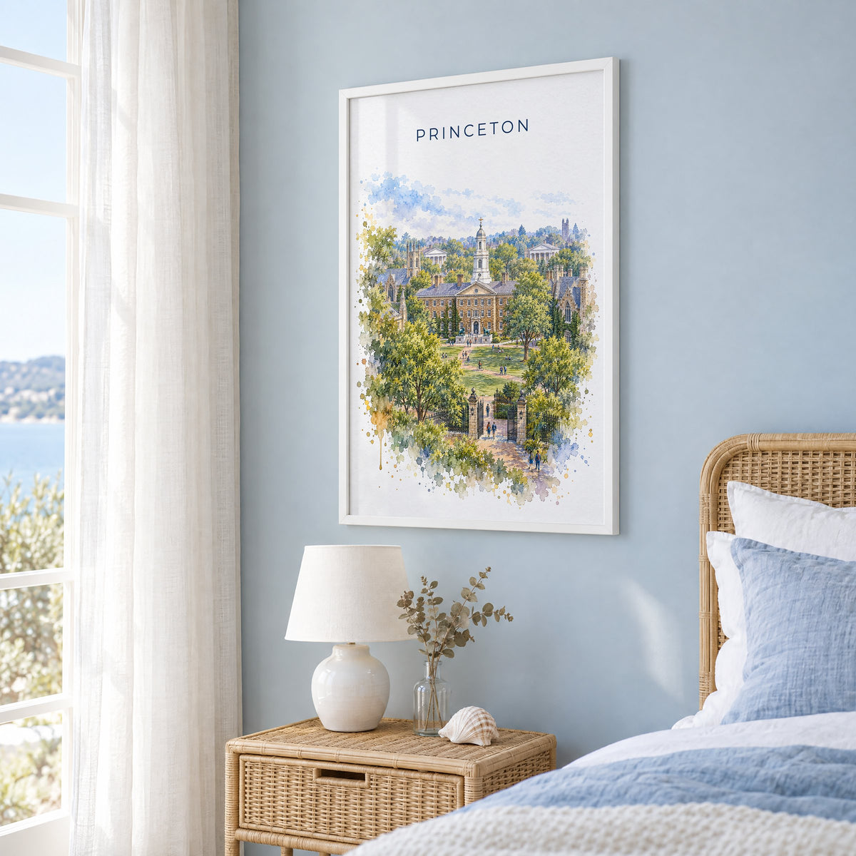 Princeton watercolor print in a white frame on a pale blue wall beside a rattan bed in a coastal bedroom