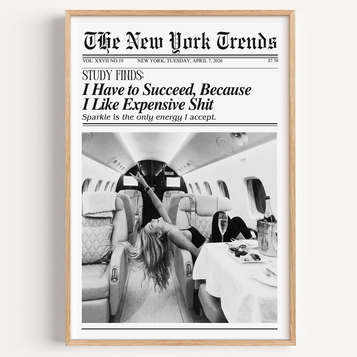 Woman with champagne in private jet mock newspaper print in a light oak frame on a plain white wall