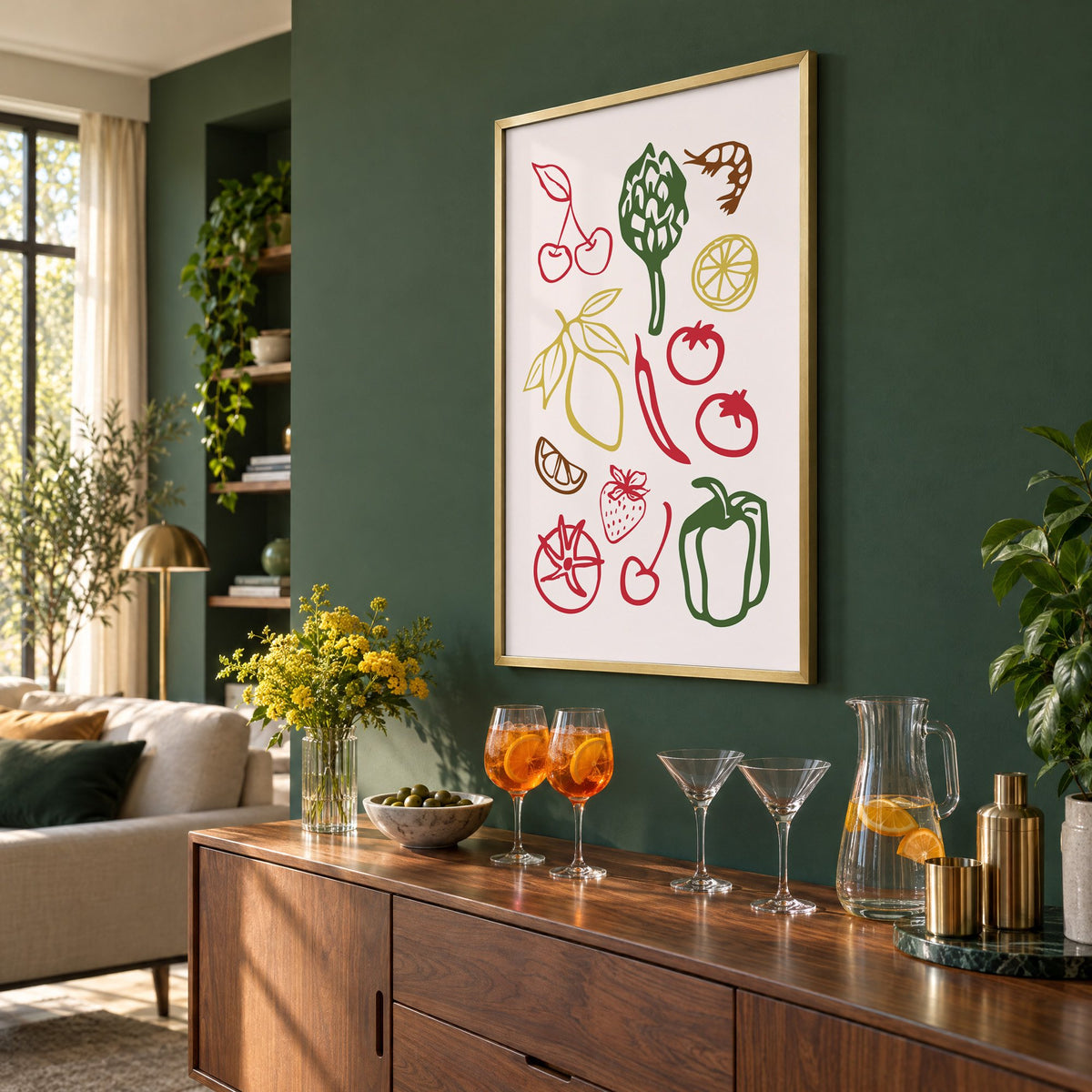 Multicolor produce doodle pattern print in a brass frame on a bottle green wall above a sideboard with spritz and martini glasses, seen at an angle
