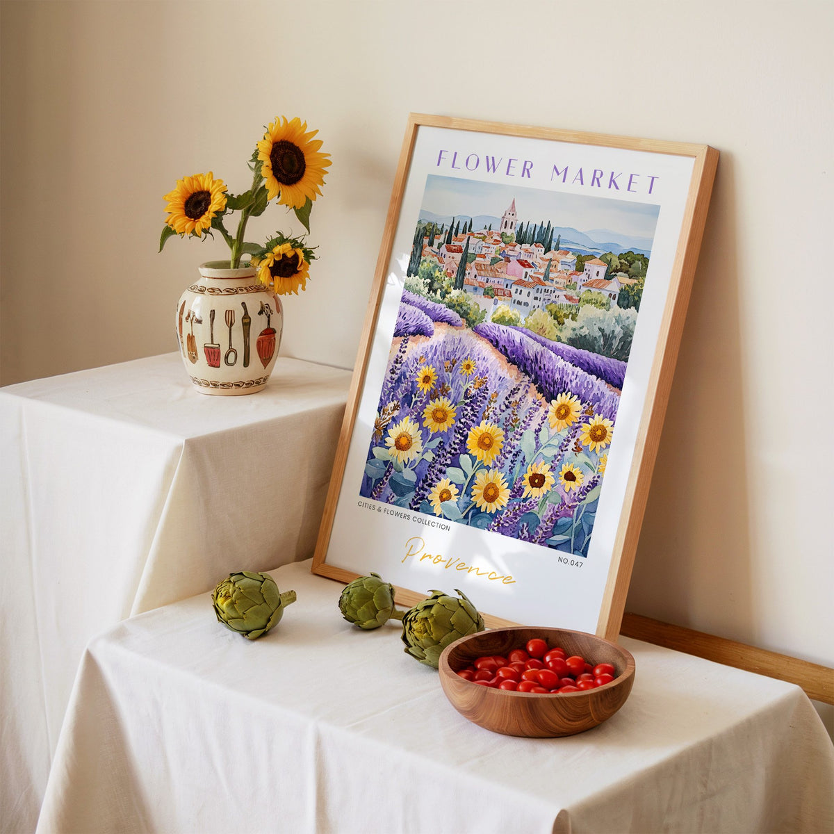 Provence flower market print in an oak frame leaning on a linen-draped table beside a vase of sunflowers
