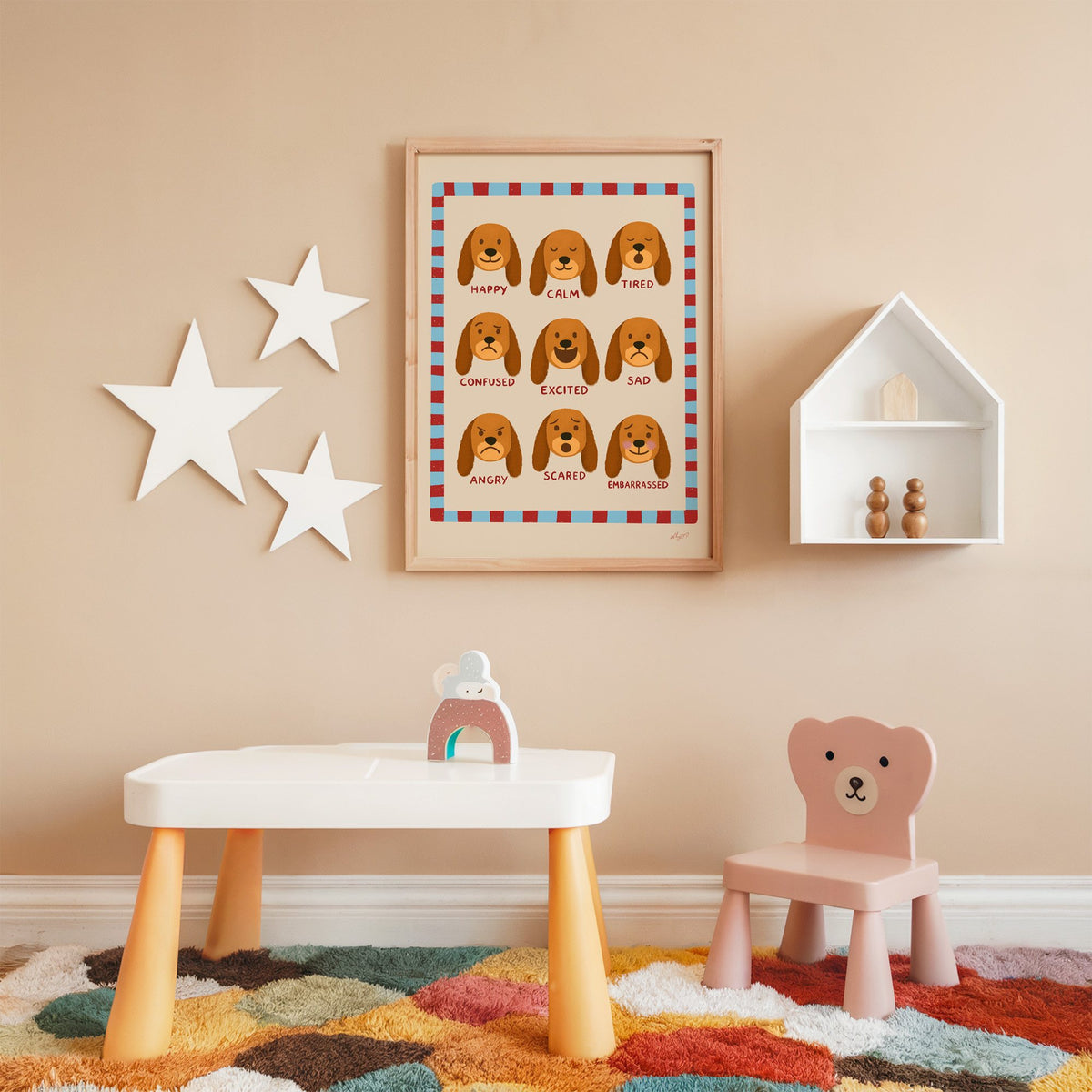 Puppy feelings chart nursery print in an oak frame on a peach wall above a kids table with wall stars
