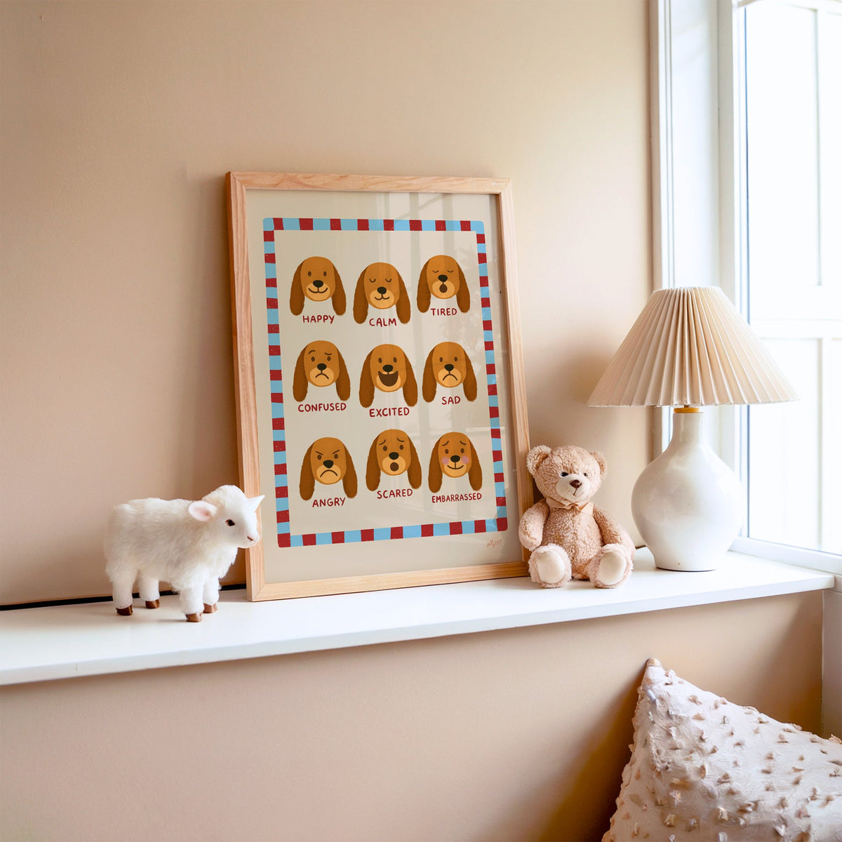 Puppy feelings chart nursery print in an oak frame on a window ledge with a toy lamb and teddy