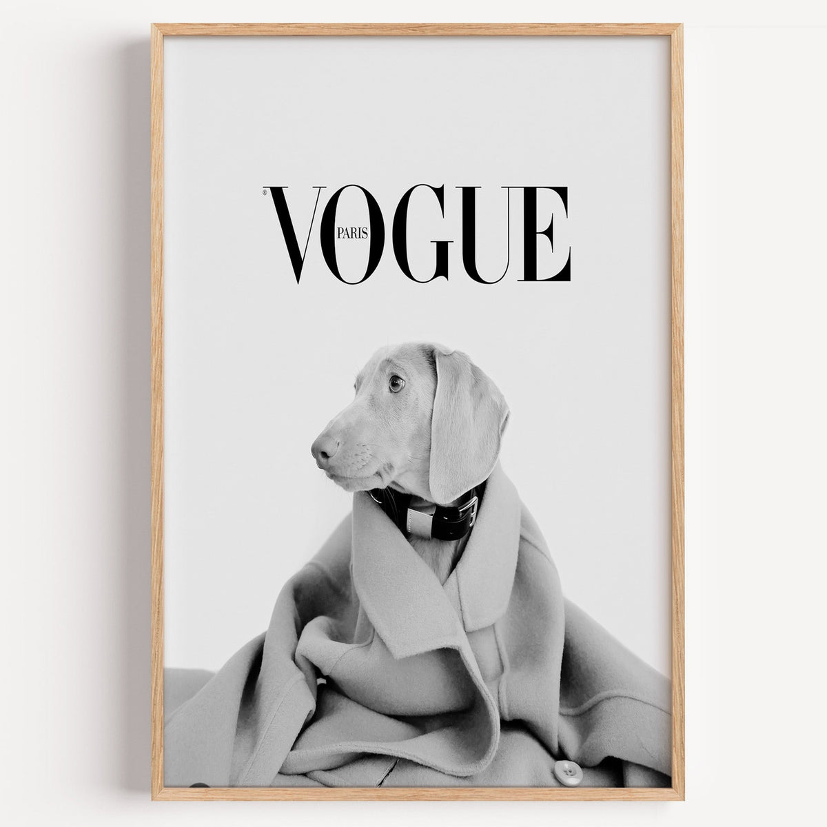 Puppy in oversized wool coat magazine cover print in a light oak frame on a plain white wall