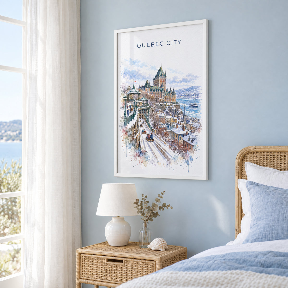 Quebec City watercolor print in a white frame on a pale blue wall beside a rattan bed in a coastal bedroom