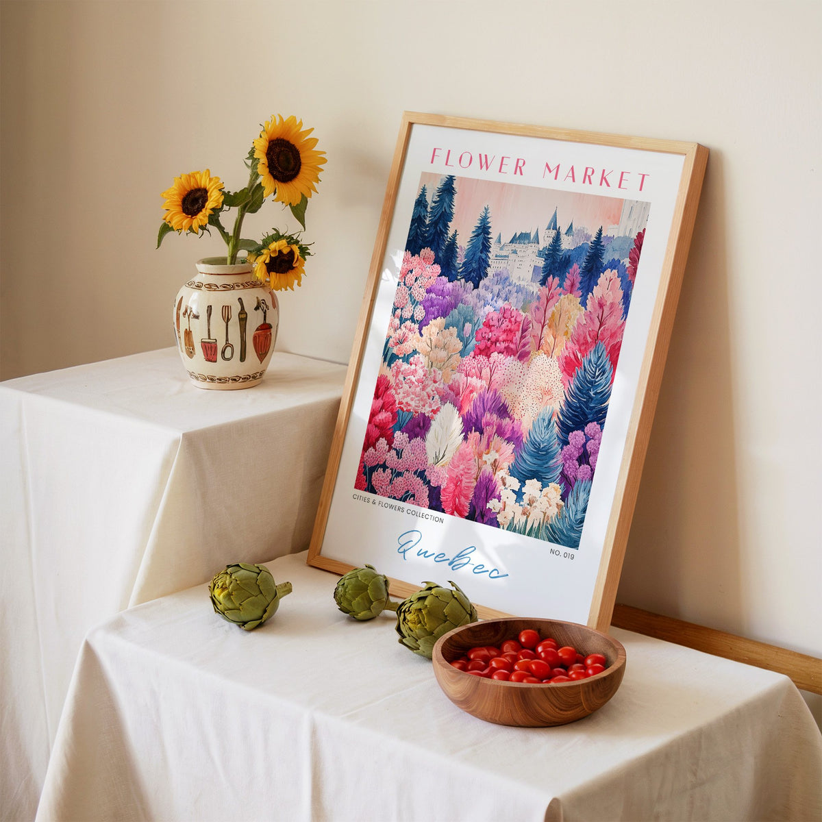 Quebec flower market print in an oak frame leaning on a linen-draped table beside a vase of sunflowers