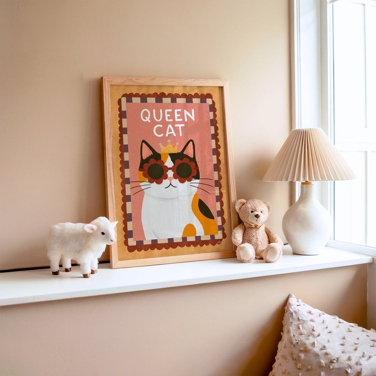 Calico cat with gold crown nursery print in an oak frame on a window ledge with a toy lamb and teddy