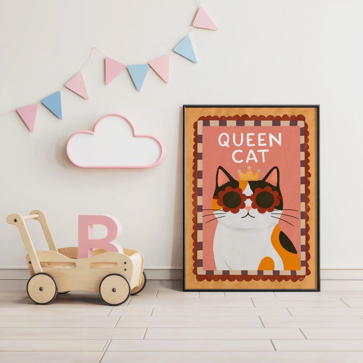 Calico cat with gold crown nursery print in a black frame under pastel bunting by a wooden baby walker