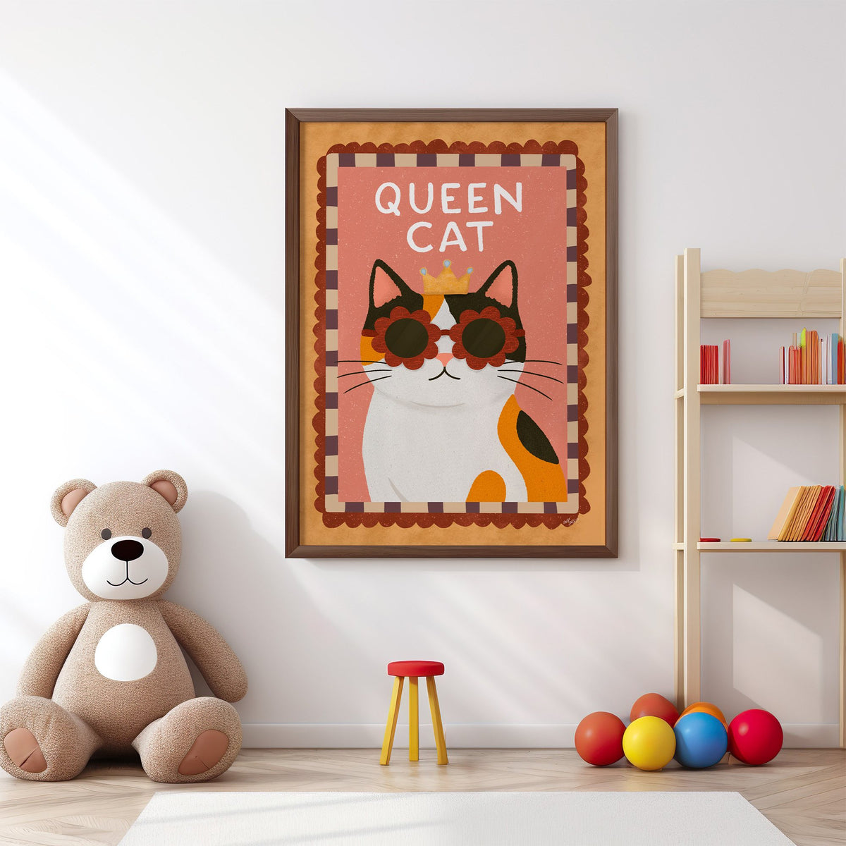 Calico cat with gold crown nursery print in a walnut frame above a big teddy bear by a bookshelf