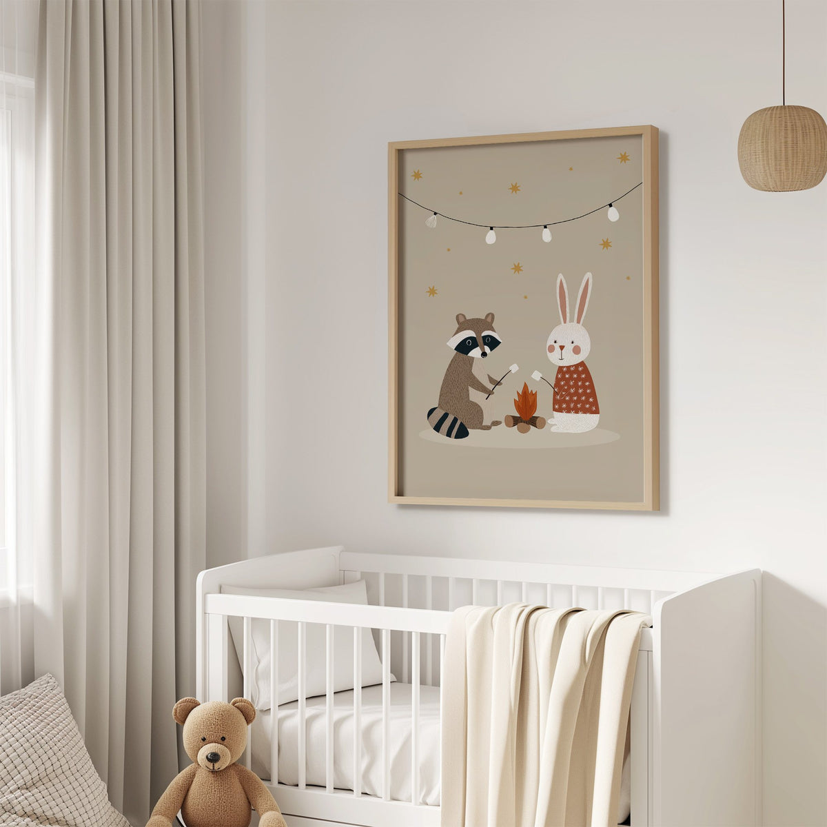 Raccoon and bunny campfire nursery print in an oak frame above a white crib with a teddy bear