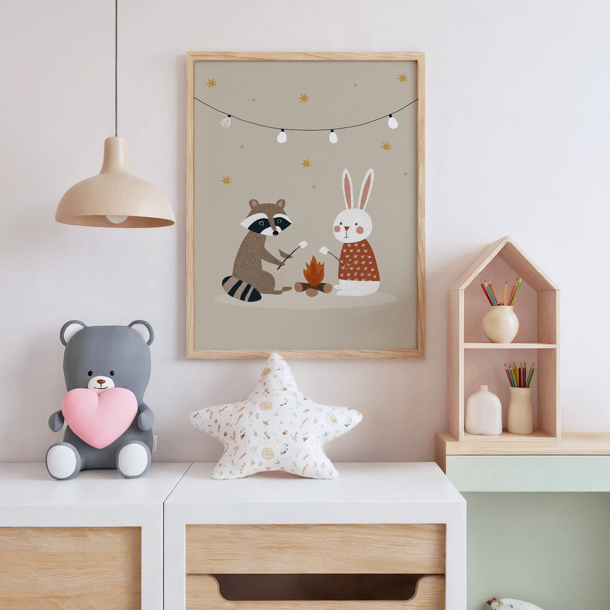 Raccoon and bunny campfire nursery print in an oak frame above a white dresser with a star pillow and house shelf