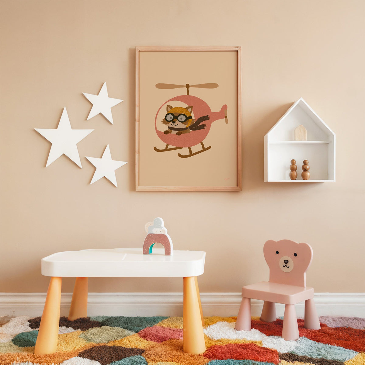 Raccoon pilot in pink helicopter nursery print in an oak frame on a peach wall above a kids table with wall stars
