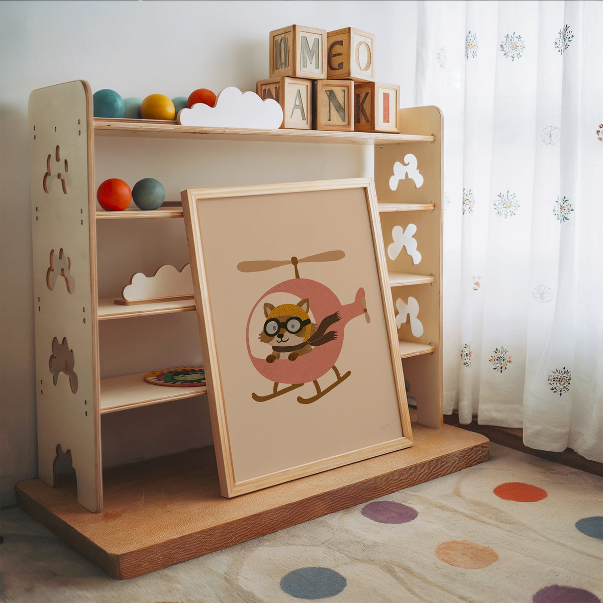 Raccoon pilot in pink helicopter nursery print in an oak frame leaning on a toy shelf with wooden letter blocks