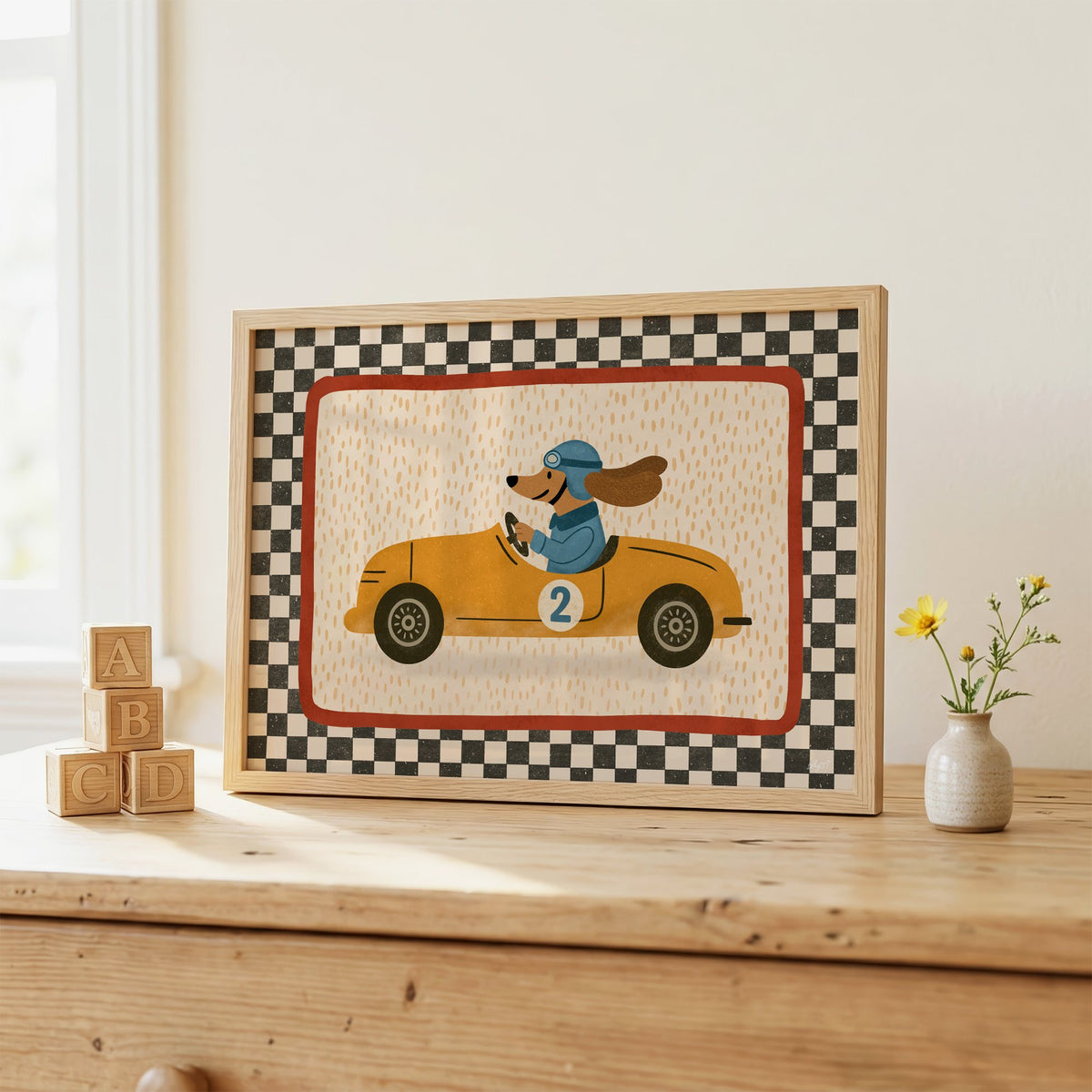 Dog driving yellow race car nursery print in an oak frame on a wooden dresser beside ABC blocks