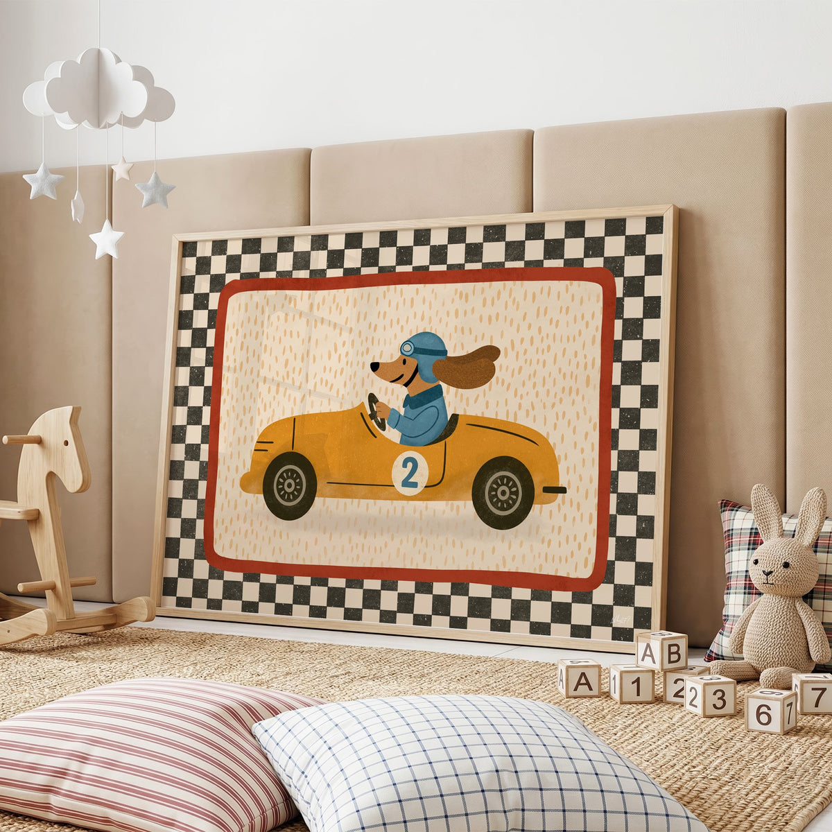 Dog driving yellow race car nursery print in an oak frame on a padded wall by a wooden rocking horse