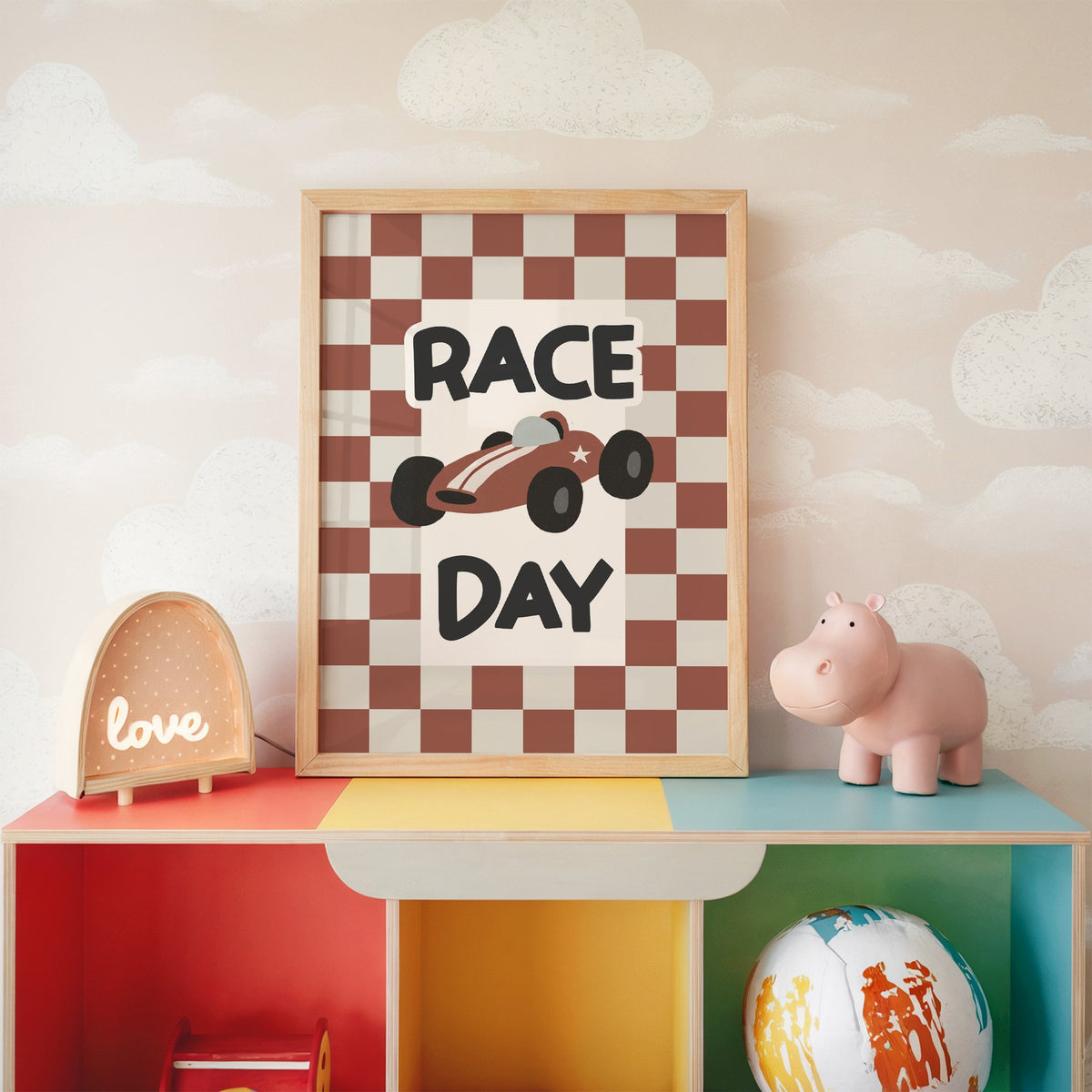 Race day red checkered nursery print in an oak frame on a rainbow toy shelf against cloud wallpaper
