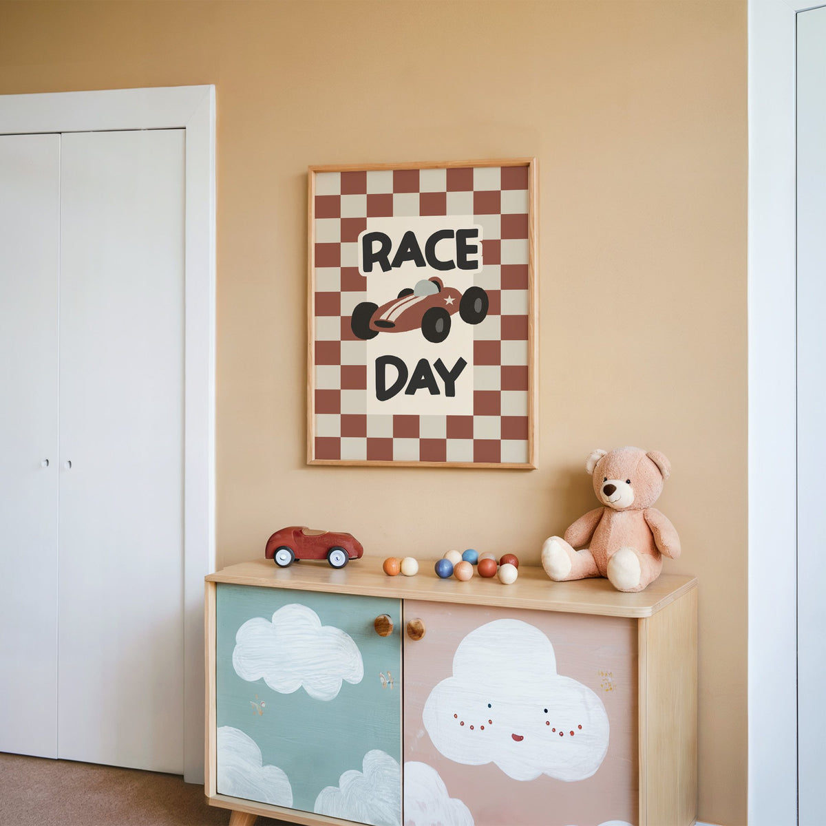 Race day red checkered nursery print in an oak frame on a peach wall above a cloud-painted cabinet