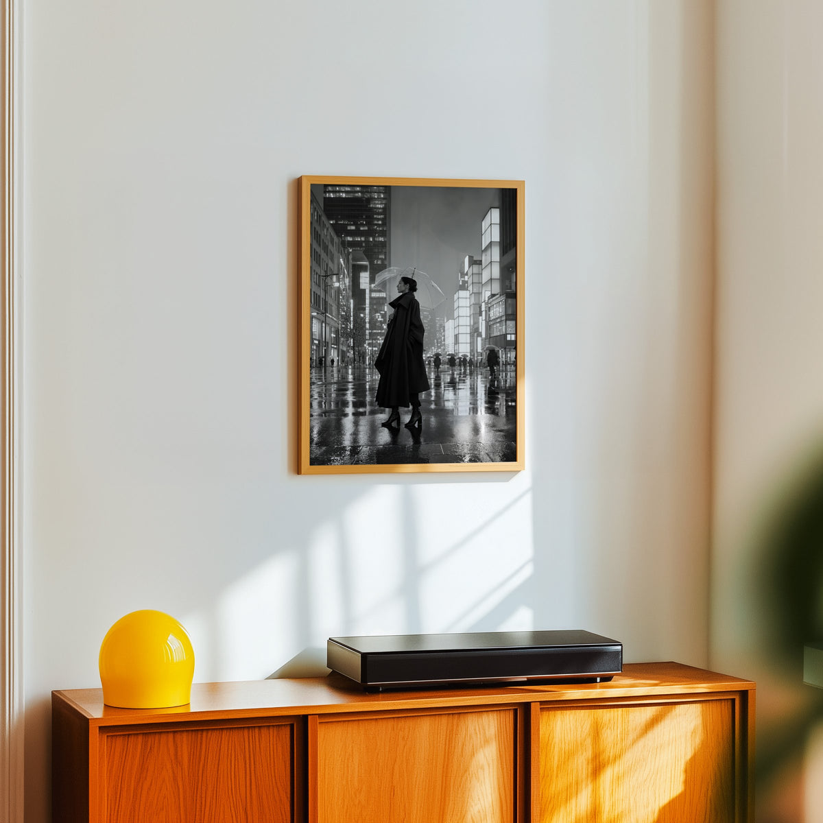 Woman with clear umbrella on rainy night street print in an oak frame above a teak sideboard with a yellow glass lamp