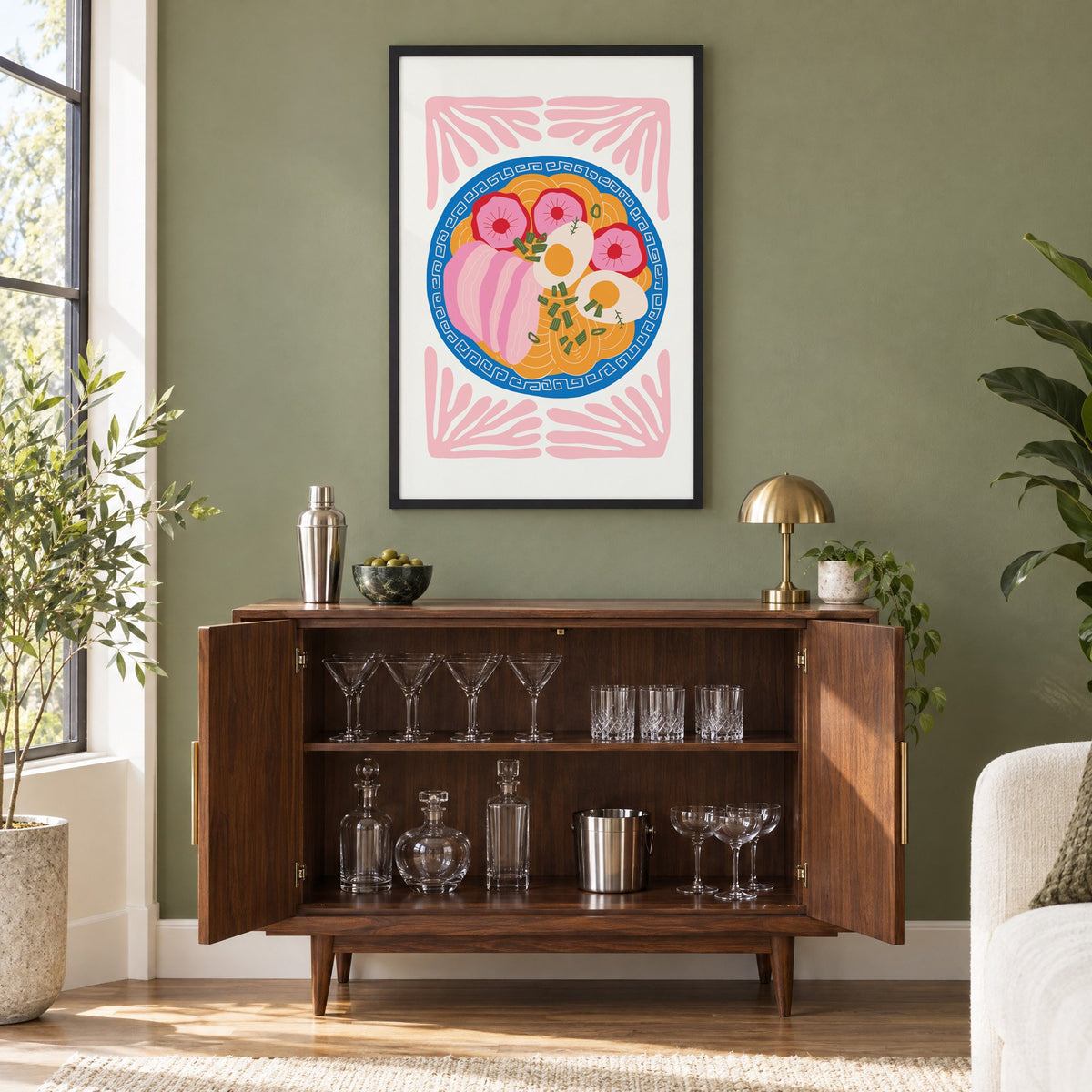 ramen bowl top view pink leaf frame print in a black frame on an olive green wall above a walnut bar cabinet with glassware