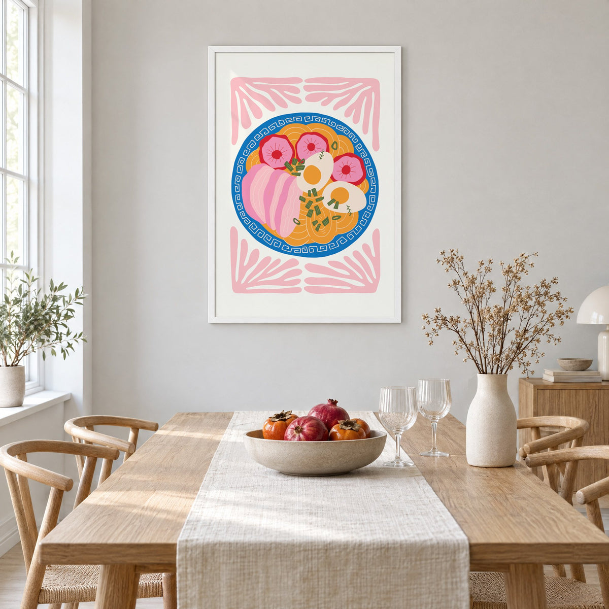 ramen bowl top view pink leaf frame print in a white frame above a light oak dining table with a linen runner and fruit bowl
