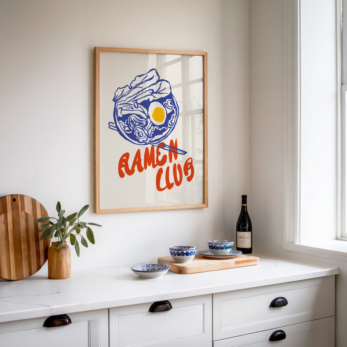 Ramen Club blue broth print in an oak frame above a white kitchen sideboard