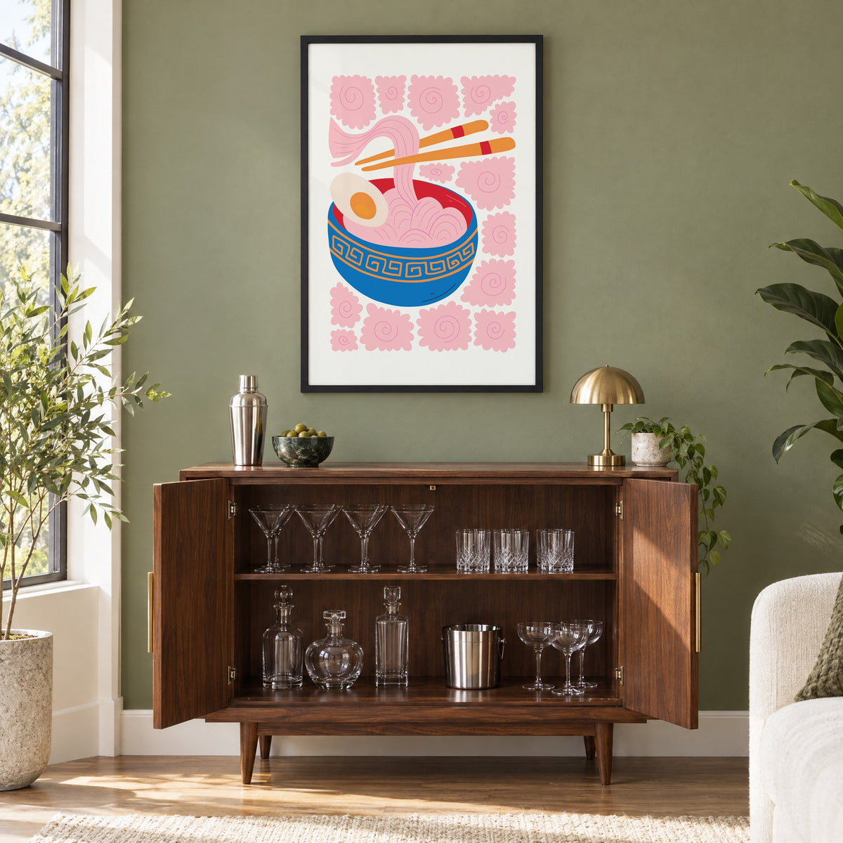 ramen noodles chopsticks pink swirl print in a black frame on an olive green wall above a walnut bar cabinet with glassware