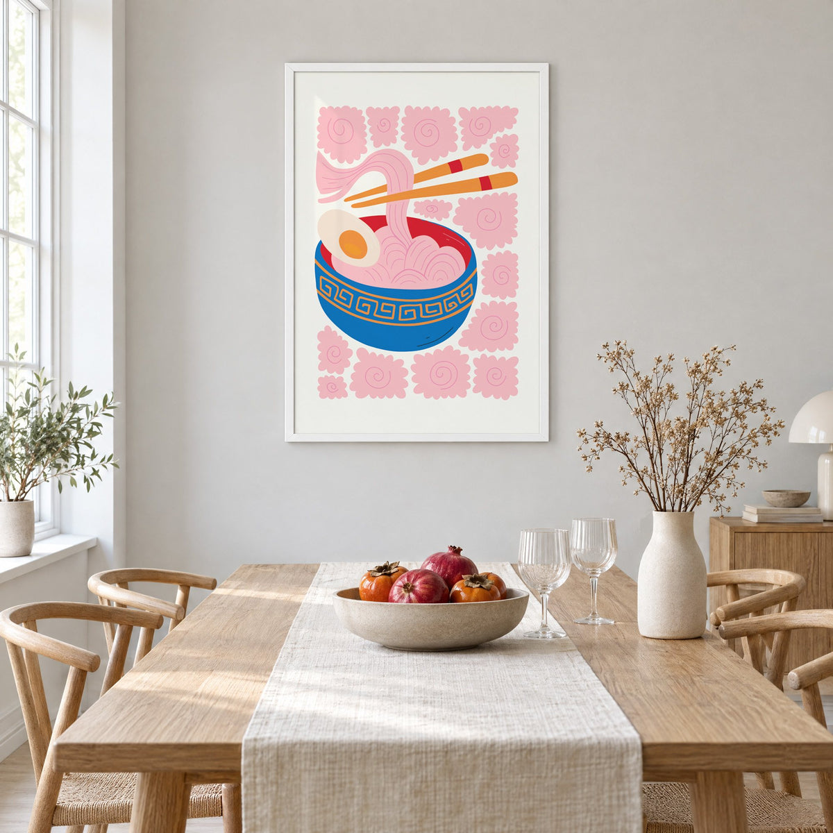 ramen noodles chopsticks pink swirl print in a white frame above a light oak dining table with a linen runner and fruit bowl