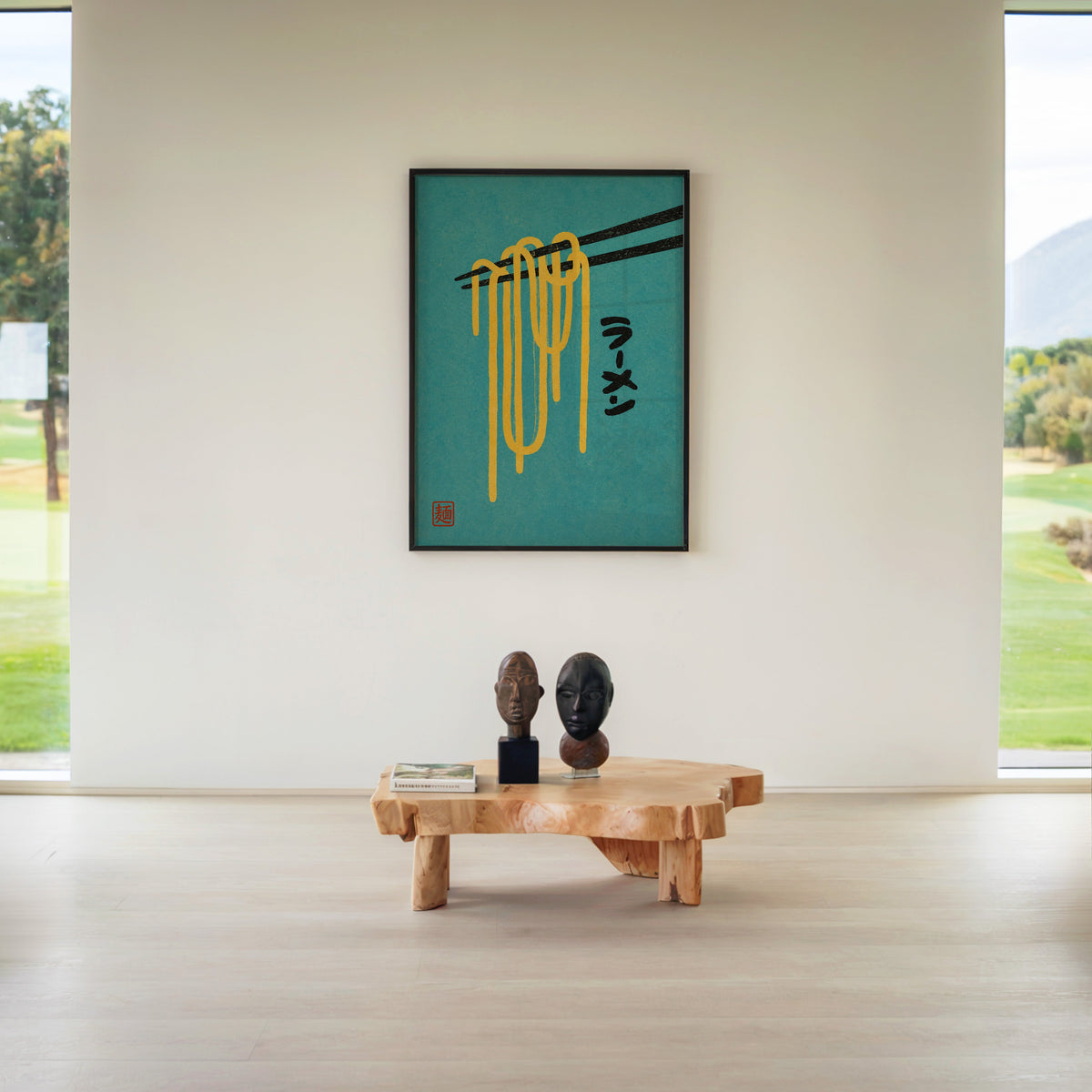 ramen noodles and chopsticks on teal print in a black frame above a live-edge wood coffee table between garden windows