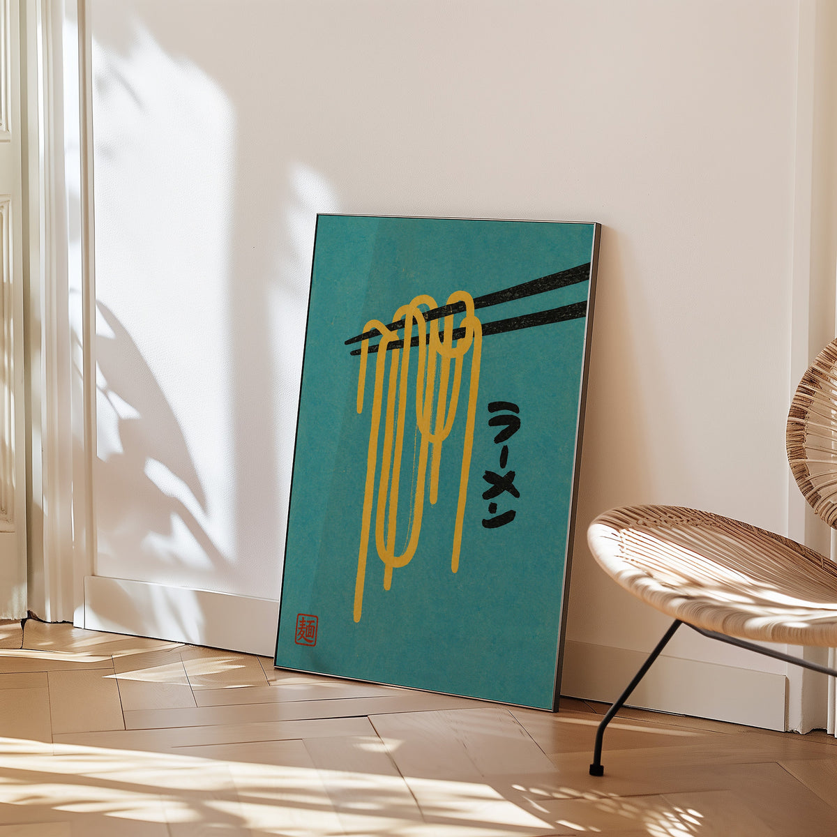 ramen noodles and chopsticks on teal print in a black frame leaning on a herringbone floor beside a woven rattan chair