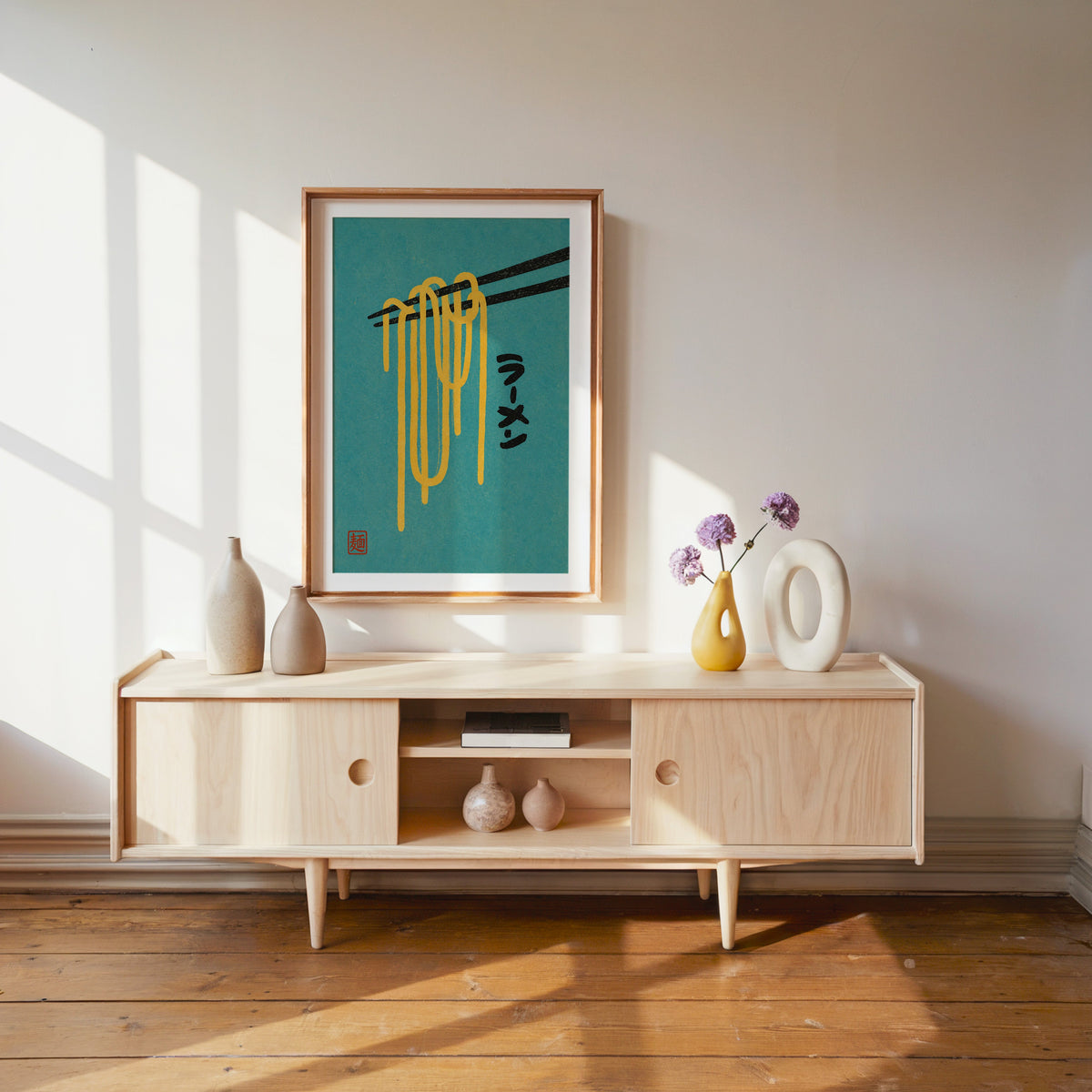 ramen noodles and chopsticks on teal print shown in a wood frame with a white mat above a pale wood media console