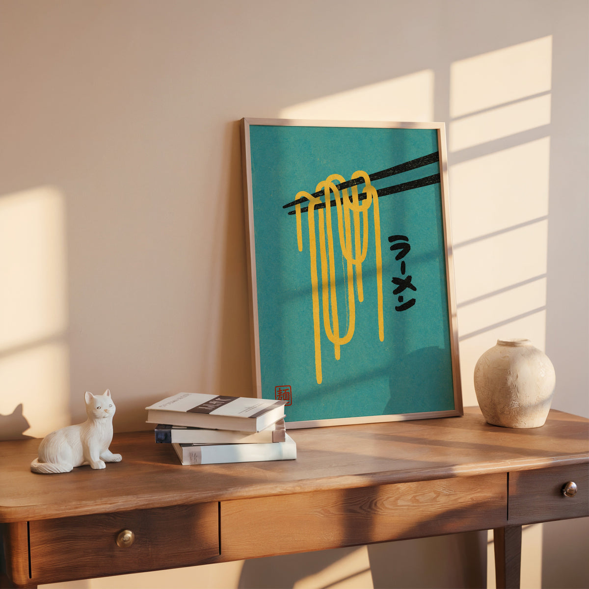 ramen noodles and chopsticks on teal print shown in a rose gold frame leaning on a wooden writing desk with books