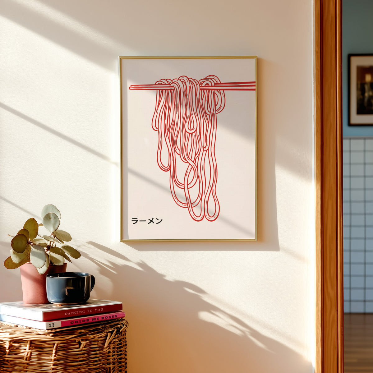 Ramen noodles print in a gold frame above a basket of books and a pilea plant