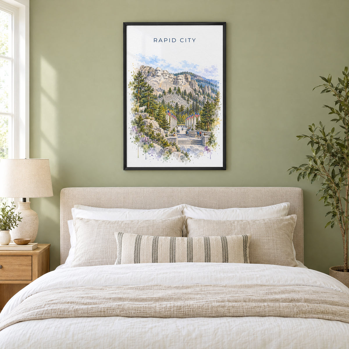 Rapid City watercolor print in a black frame above an upholstered headboard in a sage green bedroom