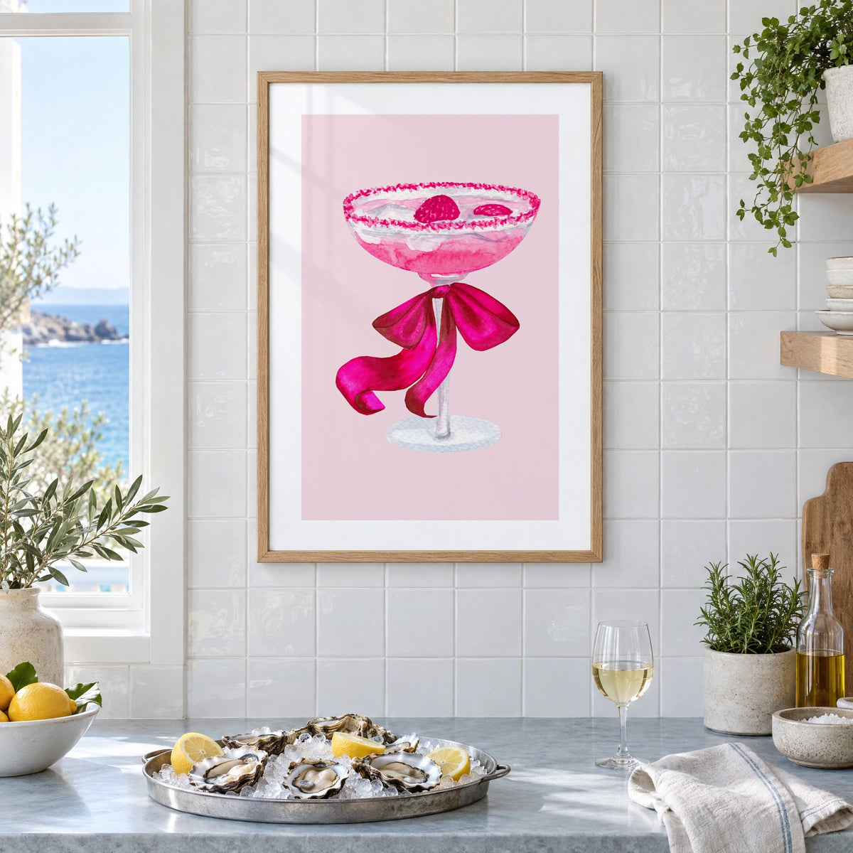 raspberry coupe magenta bow watercolor print in an oak frame on white tiles above a marble counter with oysters and lemons by a sea view