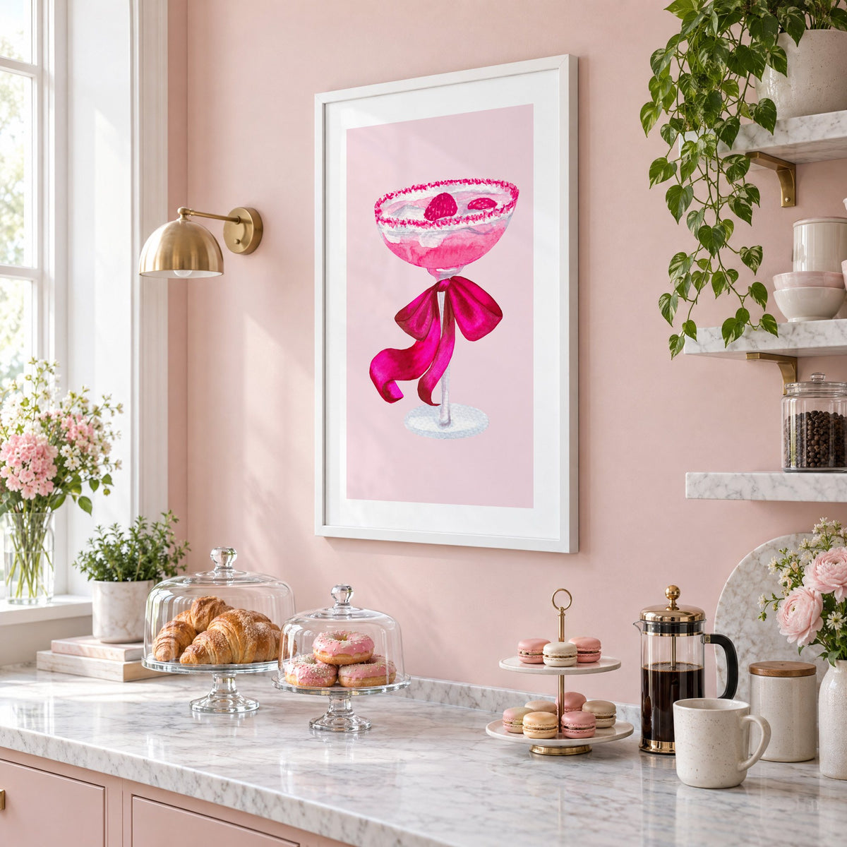 raspberry coupe magenta bow watercolor print in a white frame on a blush pink wall above a patisserie counter with croissants and macarons, seen at an angle
