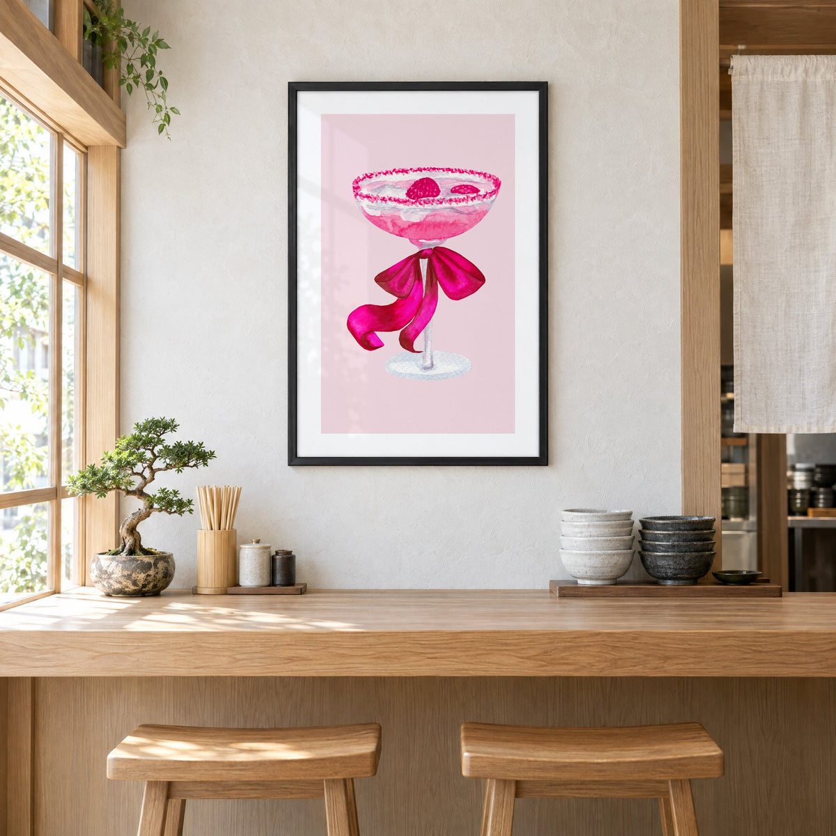 raspberry coupe magenta bow watercolor print in a black frame above a light wood ramen counter with stools and stacked bowls