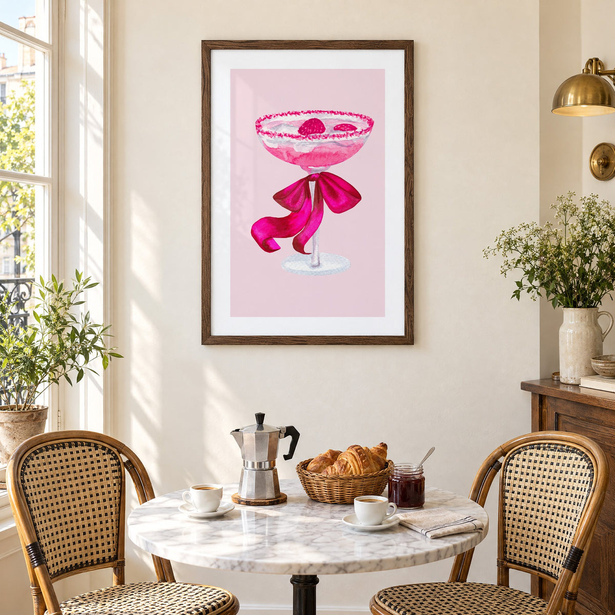 raspberry coupe magenta bow watercolor print in a walnut frame above a marble bistro table with croissants and rattan chairs
