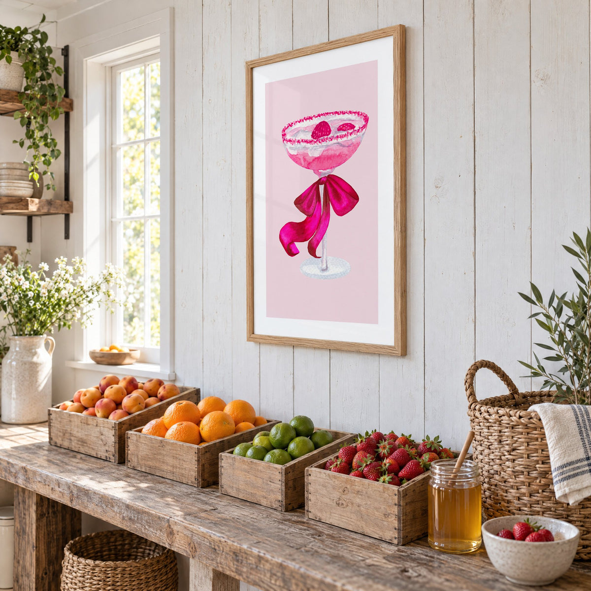 raspberry coupe magenta bow watercolor print in an oak frame on white plank walls above wooden crates of fresh fruit, seen at an angle
