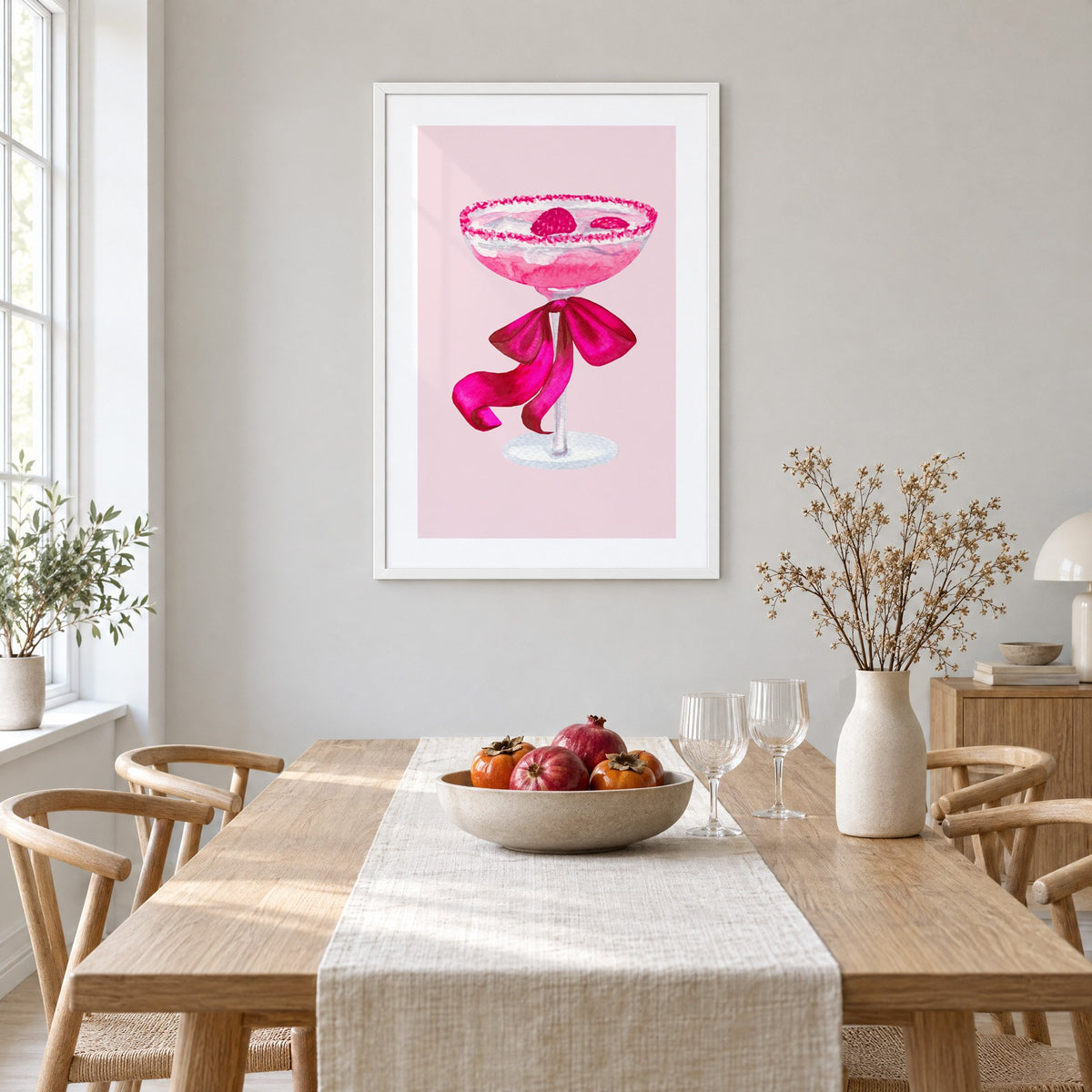 raspberry coupe magenta bow watercolor print in a white frame above a light oak dining table with a linen runner and fruit bowl