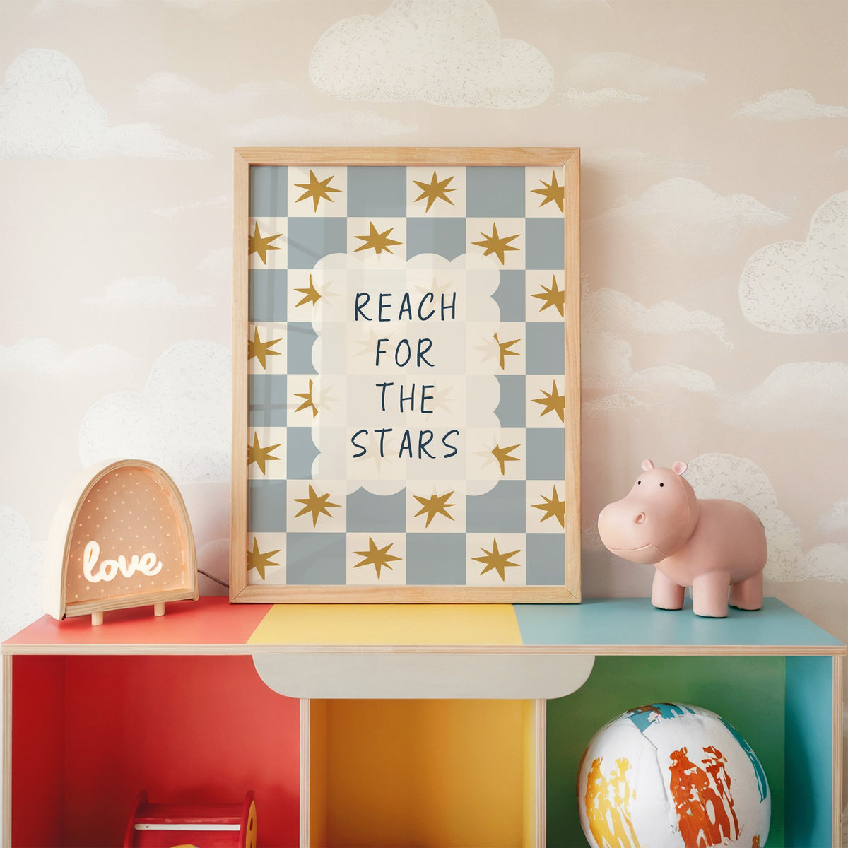 Reach for the stars cloud nursery print in an oak frame on a rainbow toy shelf against cloud wallpaper