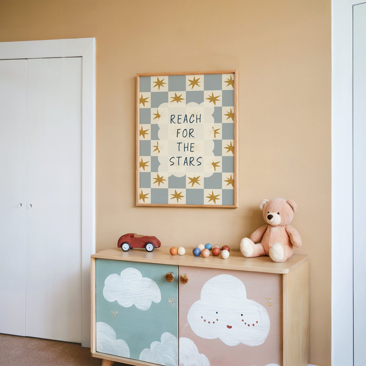 Reach for the stars cloud nursery print in an oak frame on a peach wall above a cloud-painted cabinet