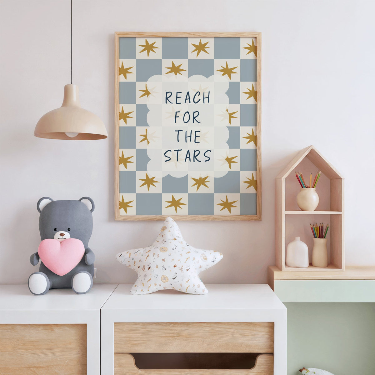 Reach for the stars cloud nursery print in an oak frame above a white dresser with a star pillow and house shelf