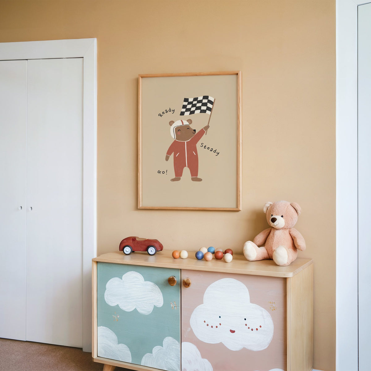 Ready steady go racing bear nursery print in an oak frame on a peach wall above a cloud-painted cabinet