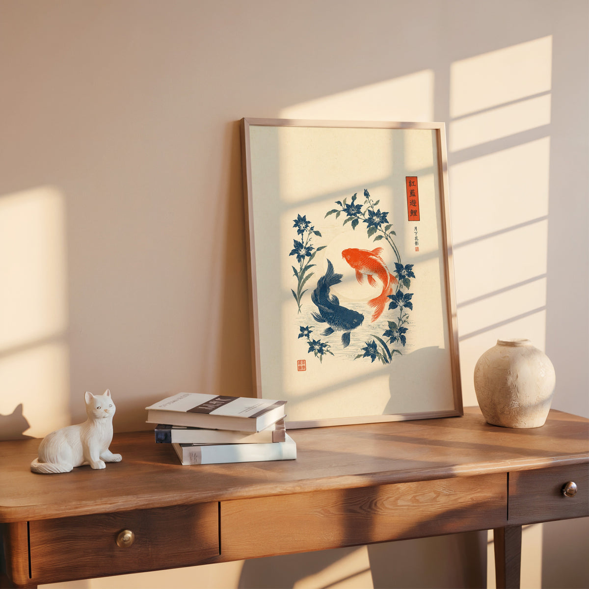 red and blue koi with blue flowers print shown in a rose gold frame leaning on a wooden writing desk with books