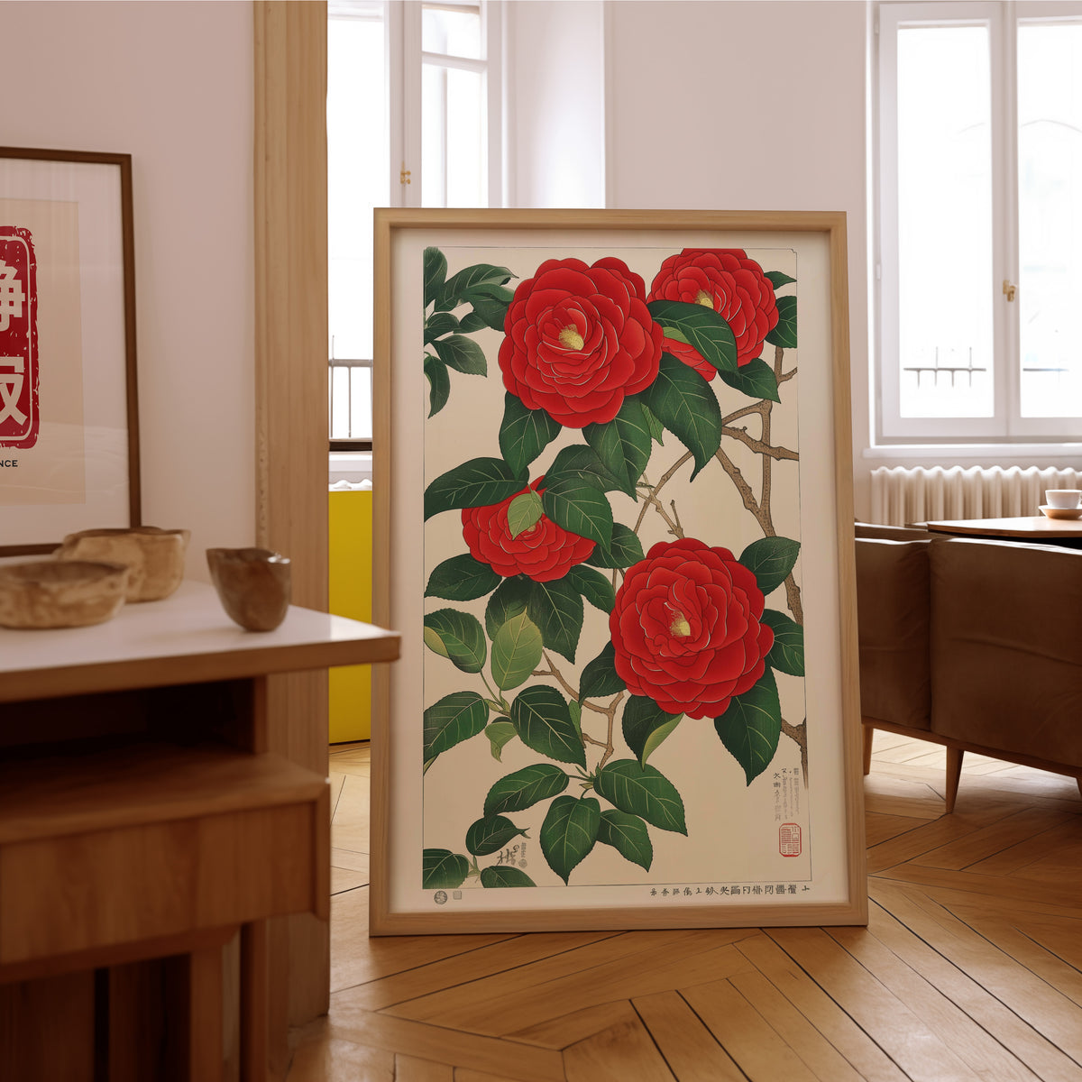Red camellia woodblock-style print in an oak frame on the parquet floor of a sunlit living room