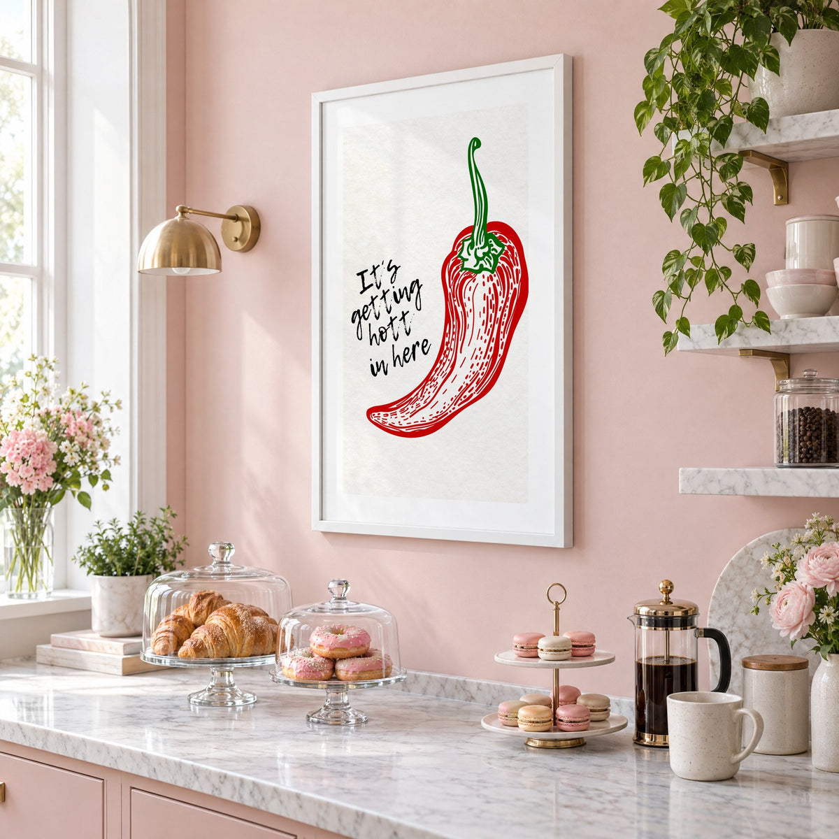 It's getting hott red chili engraving print in a white frame on a blush pink wall above a patisserie counter with croissants and macarons, seen at an angle