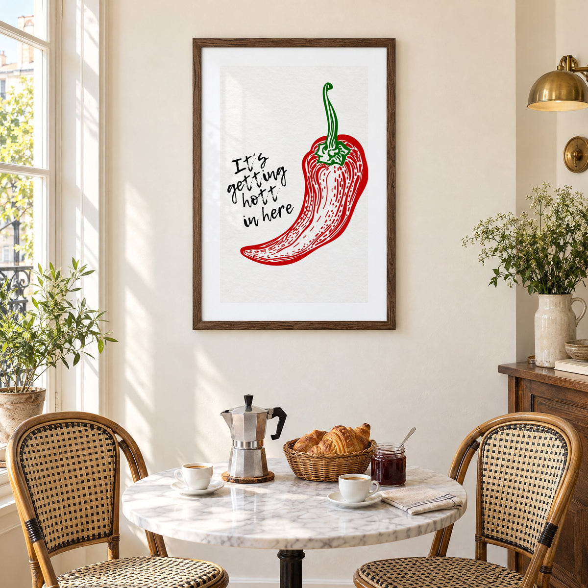 It's getting hott red chili engraving print in a walnut frame above a marble bistro table with croissants and rattan chairs