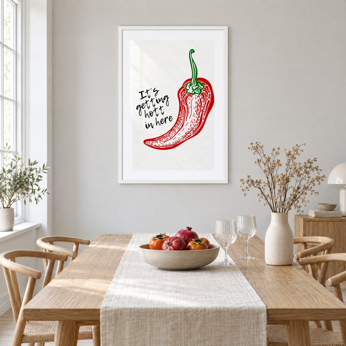 It's getting hott red chili engraving print in a white frame above a light oak dining table with a linen runner and fruit bowl