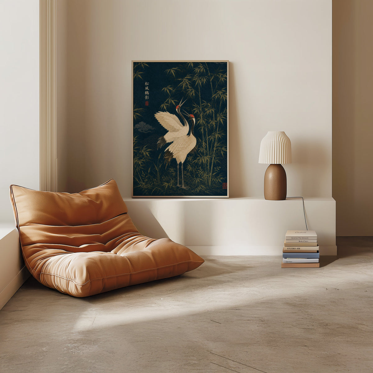 red-crowned cranes and bamboo on navy print in a light oak frame on a white ledge by a tan leather floor chair